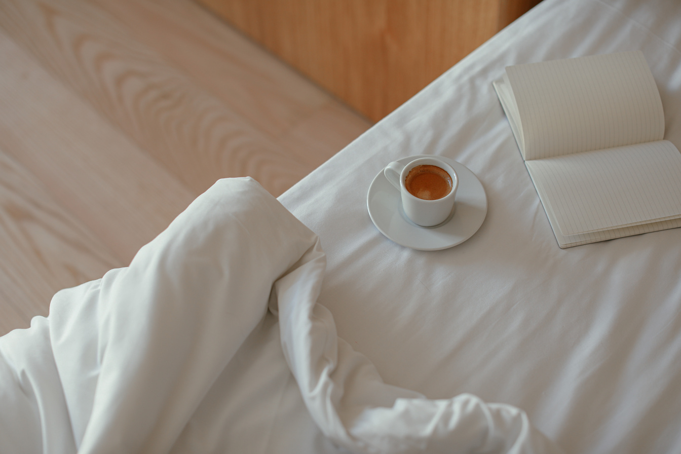 A Cup of Coffee and a Notebook on the Bed with White Linen